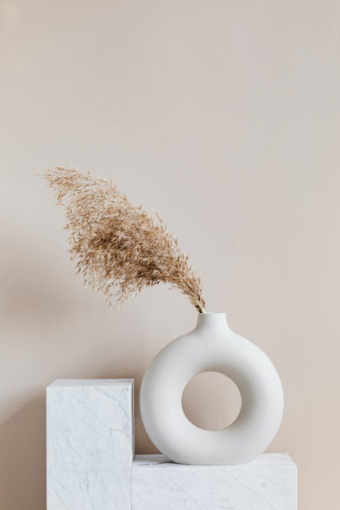 Elegant ceramic vase with dried grass on a marble pedestal, showcasing simplicity and minimalism.